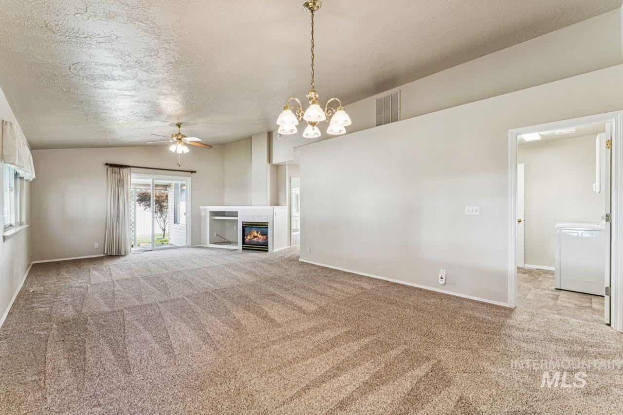 Unfurnished living room with a textured ceiling, light carpet, a ceiling fan, a glass covered fireplace, and vaulted ceiling