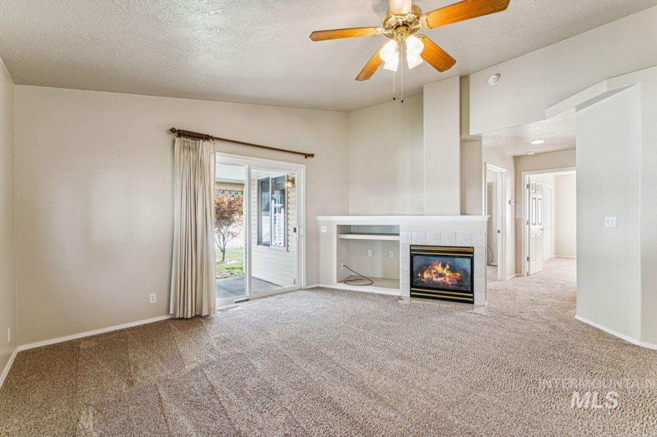 Unfurnished living room with lofted ceiling, a tile fireplace, a textured ceiling, carpet flooring, and ceiling fan