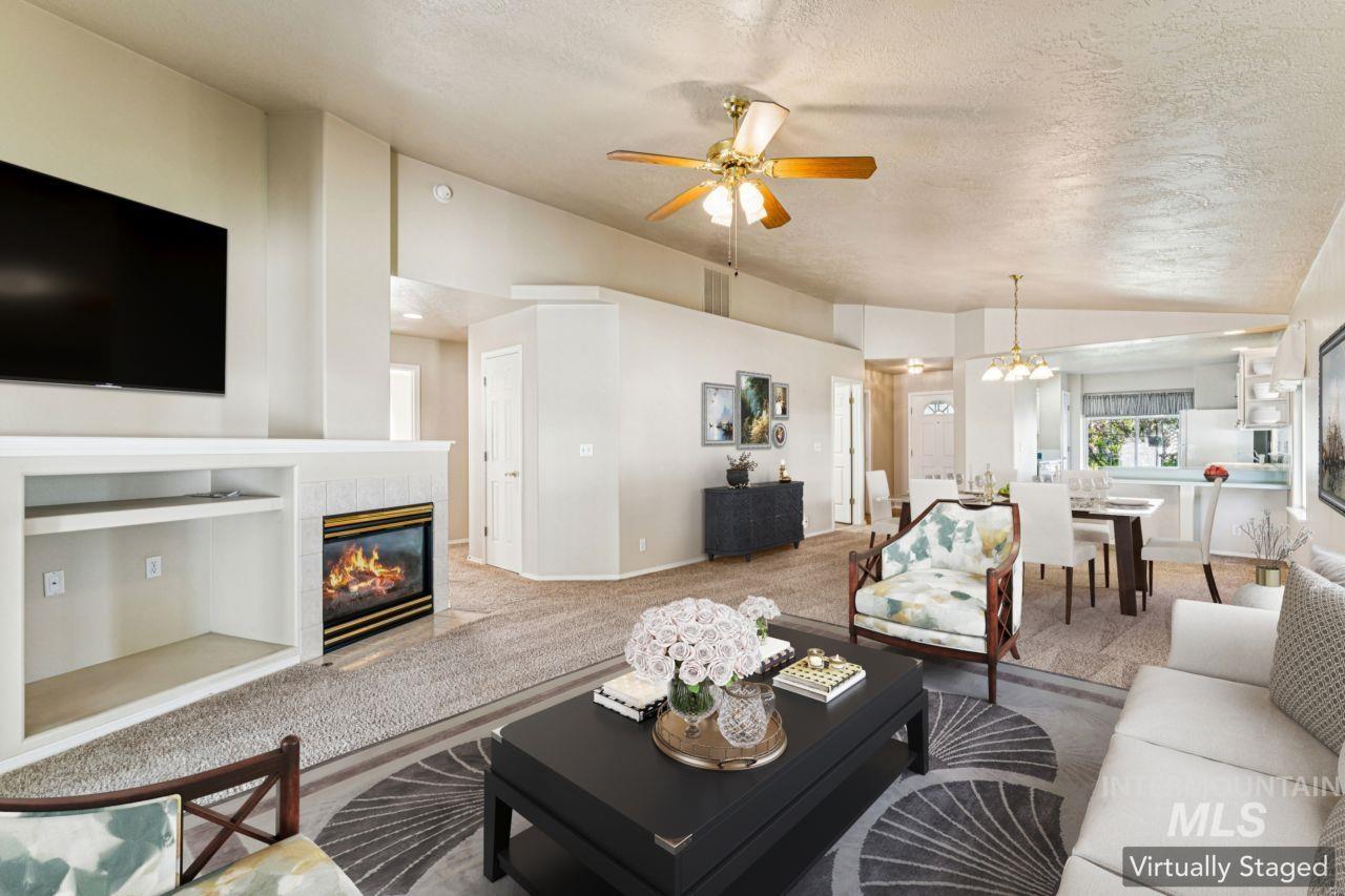 Carpeted living area with a textured ceiling, a tile fireplace, vaulted ceiling, ceiling fan, and a chandelier