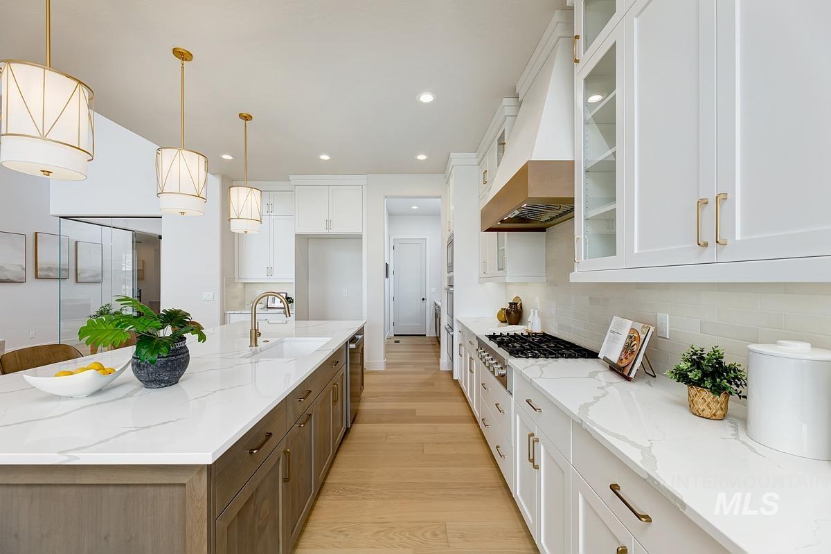 Kitchen with glass insert cabinets, light wood finished floors, light stone counters, pendant lighting, and white cabinetry