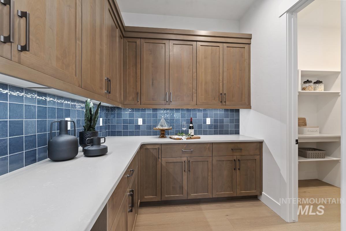 Kitchen featuring decorative backsplash, light wood-style floors, brown cabinets, and light stone countertops