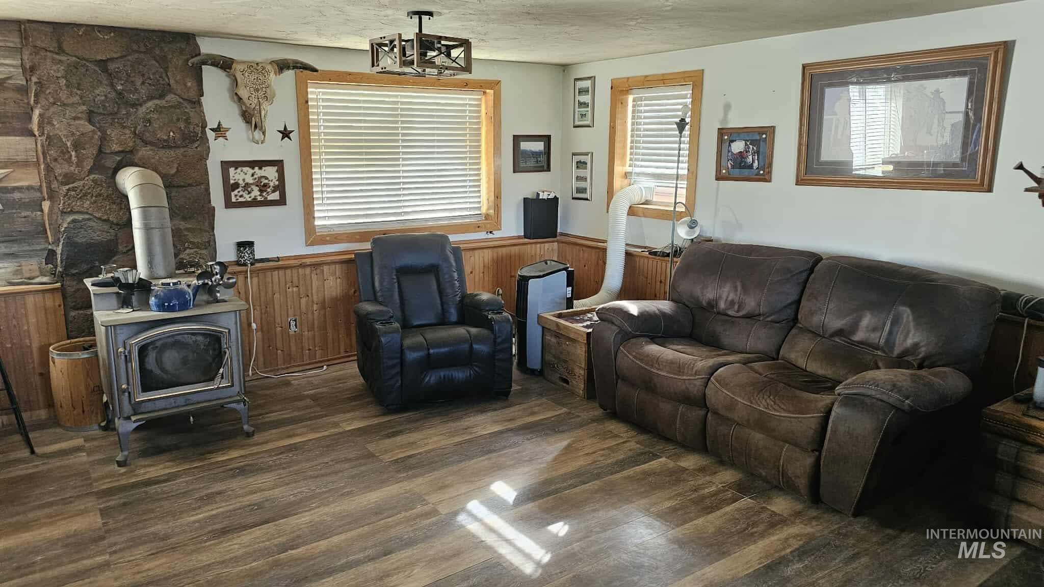 Living room featuring a wood stove, wainscoting, wood finished floors, wood walls, and a textured ceiling
