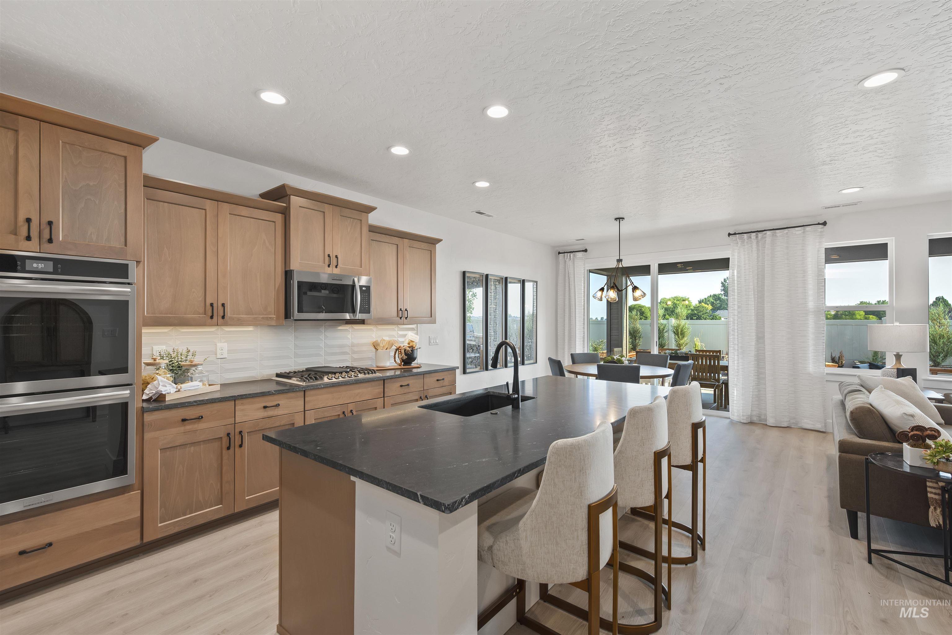 Kitchen featuring appliances with stainless steel finishes, an island with sink, dark stone counters, a kitchen breakfast bar, and tasteful backsplash