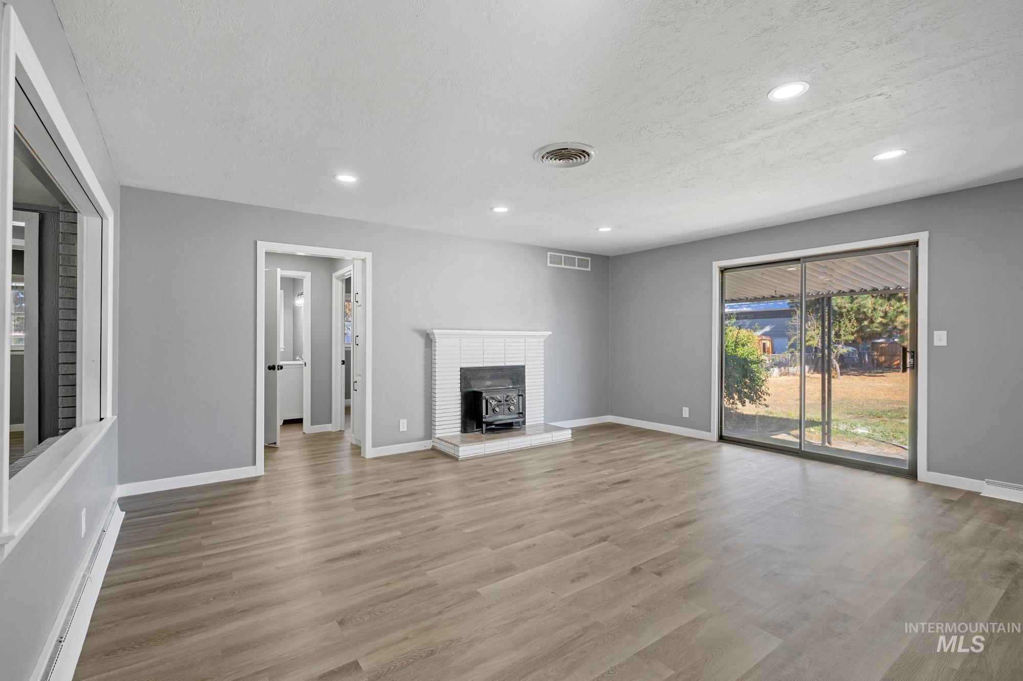 Unfurnished living room with light wood-type flooring, recessed lighting, a textured ceiling, and a wood stove