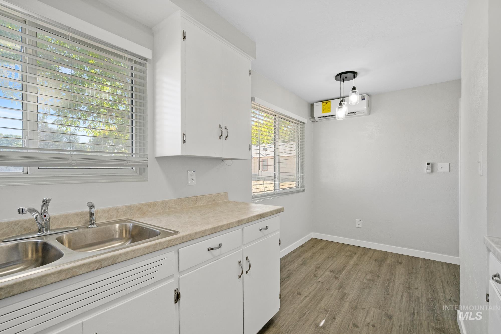 Kitchen featuring light countertops, wood finished floors, white cabinetry, a wall unit AC, and hanging light fixtures