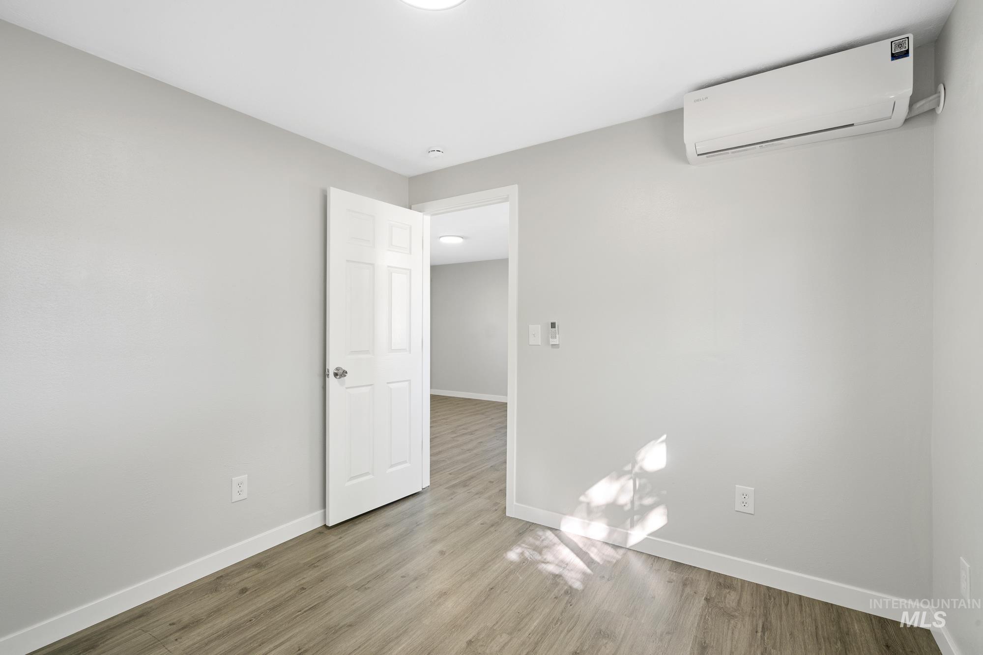 Empty room with an AC wall unit and light wood finished floors