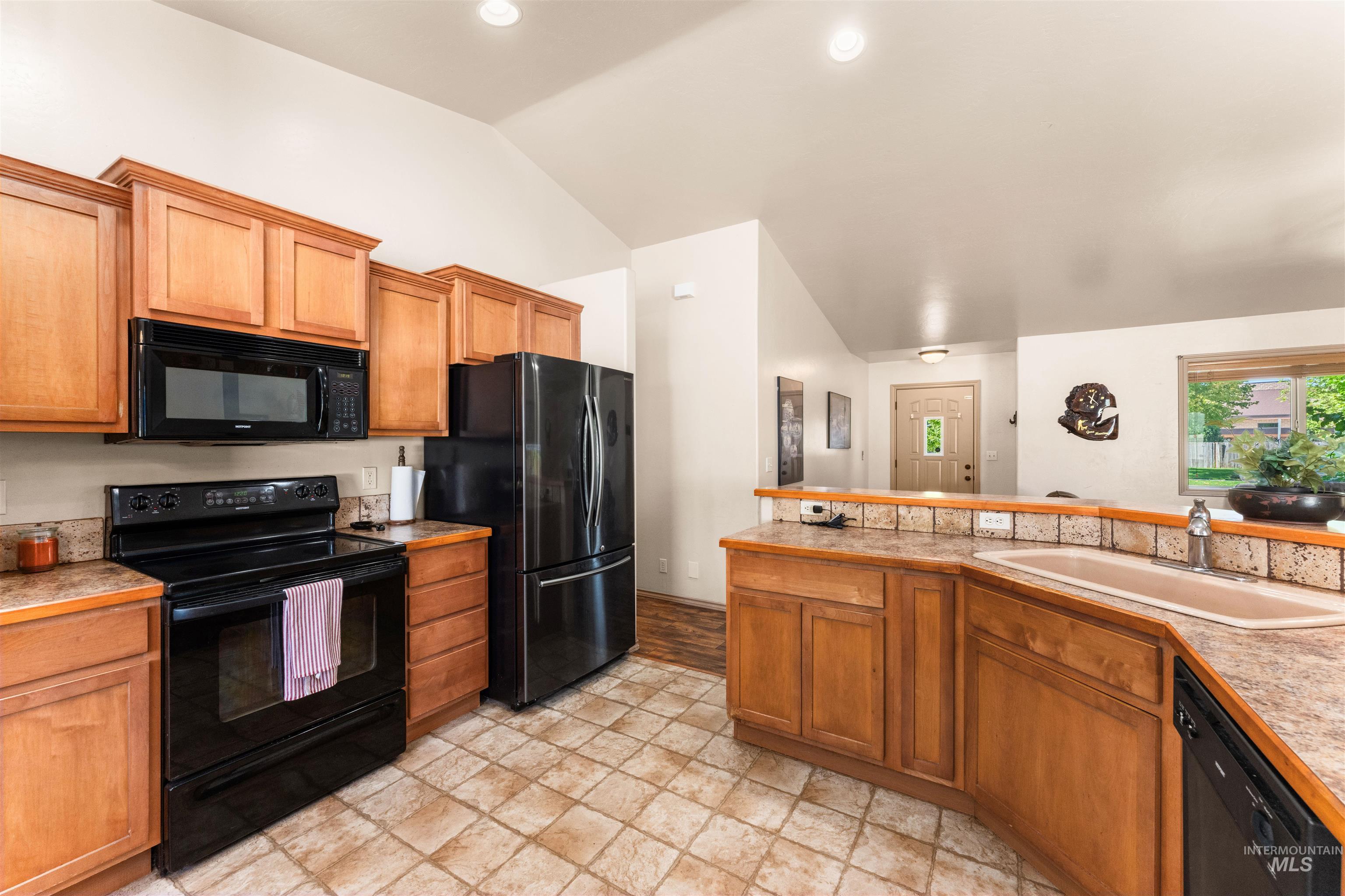 Kitchen featuring black appliances, brown cabinets, vaulted ceiling, and light countertops