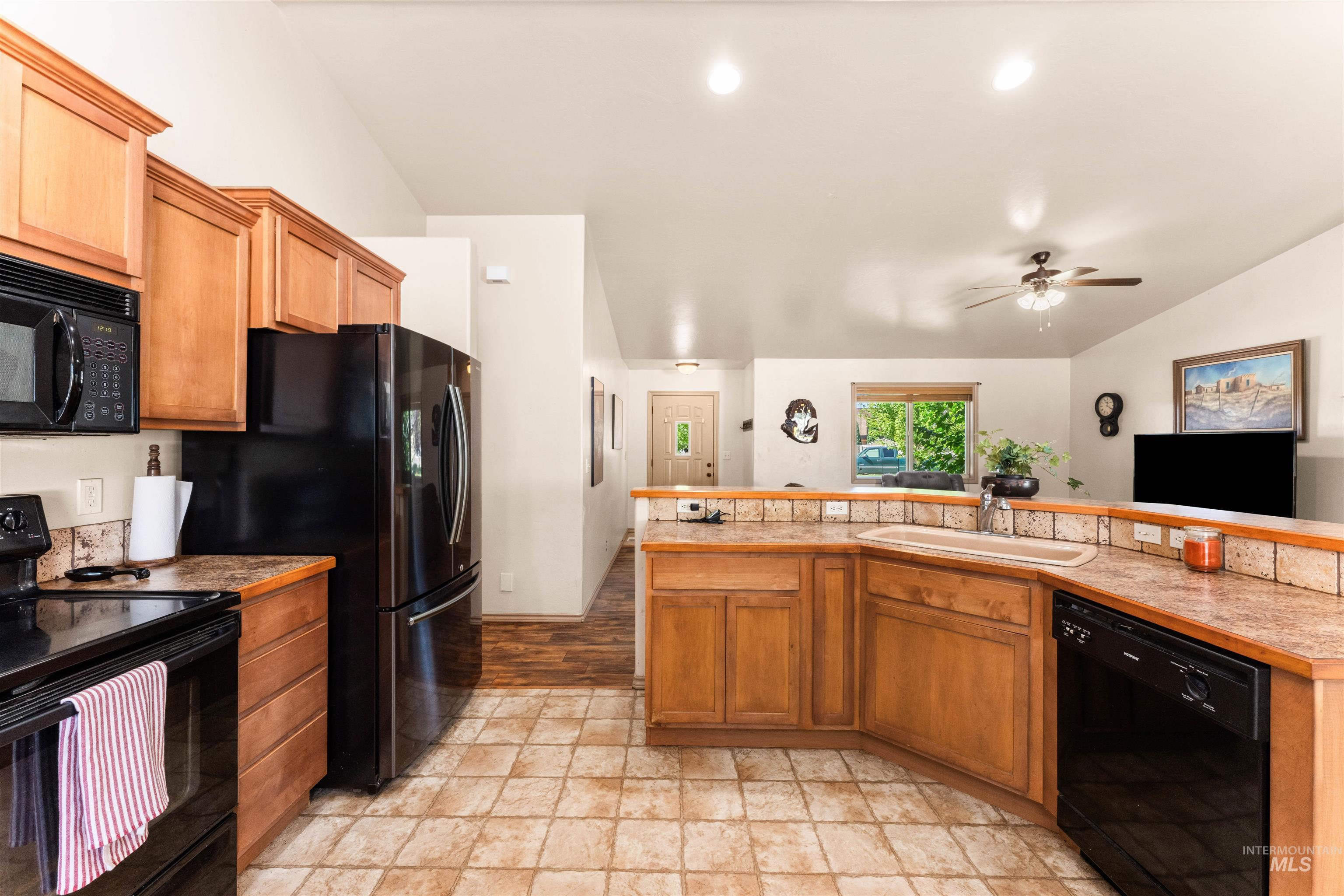 Kitchen featuring black appliances, brown cabinets, vaulted ceiling, light countertops, and ceiling fan