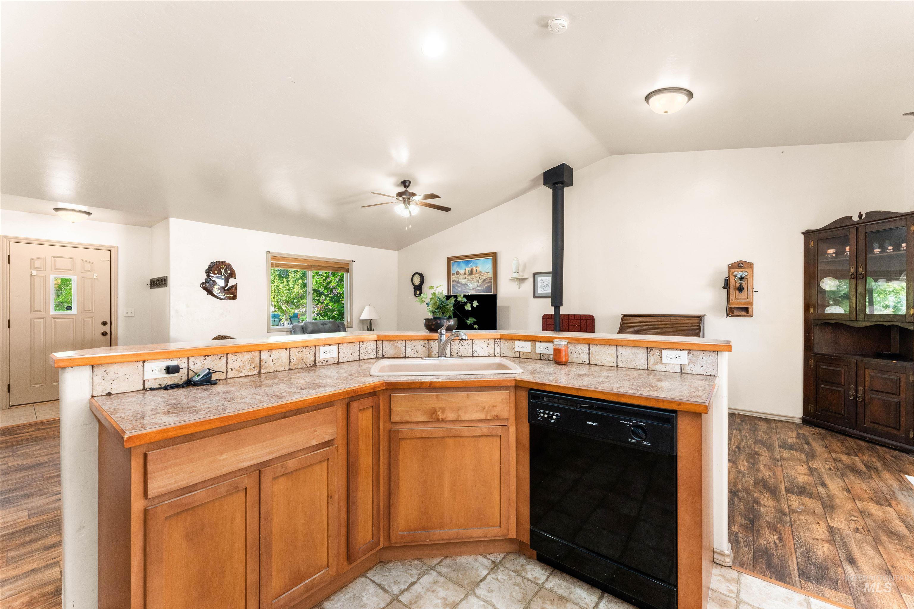 Kitchen with brown cabinets, light countertops, black dishwasher, vaulted ceiling, and light wood-style floors