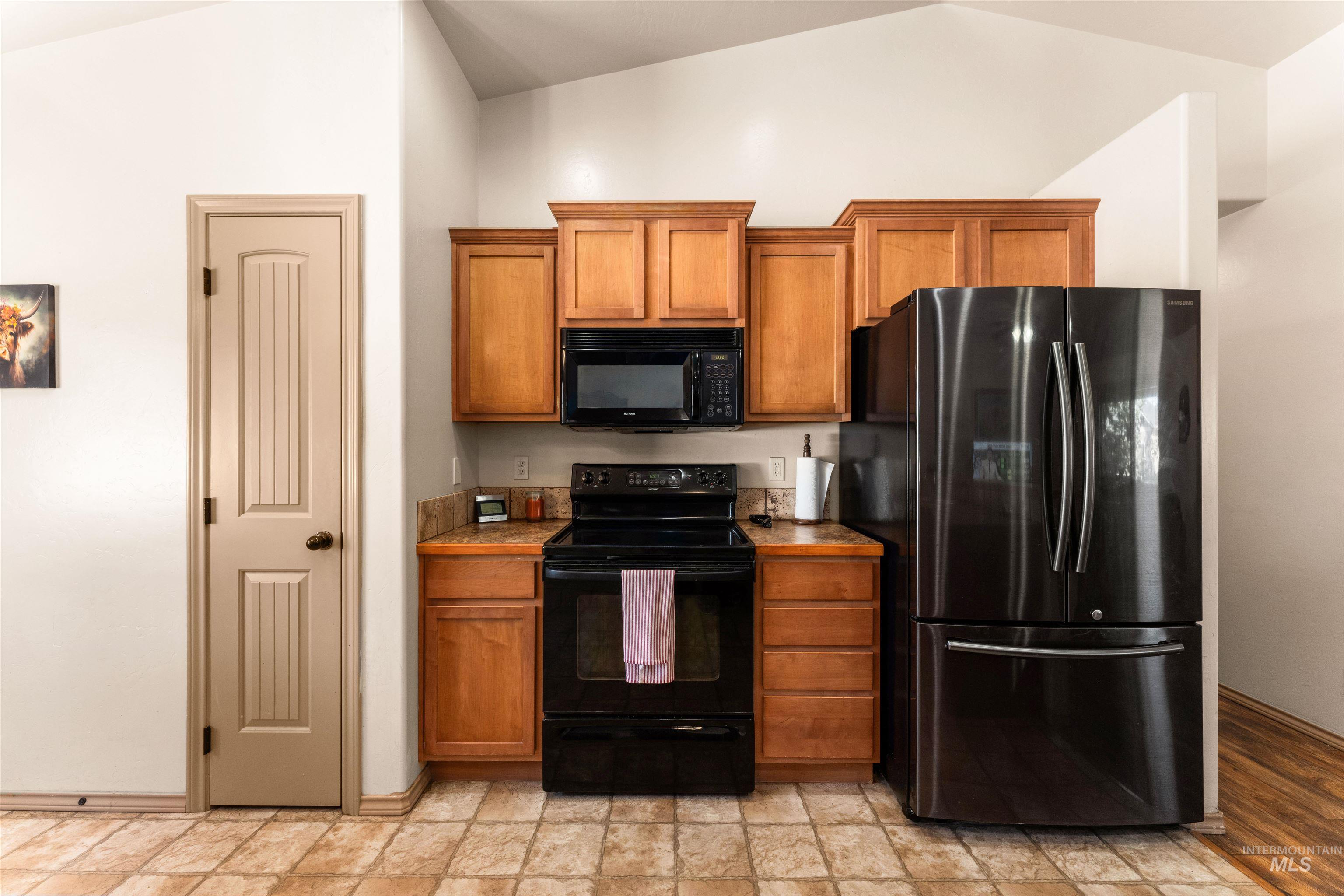 Kitchen with black appliances, brown cabinets, lofted ceiling, and light countertops