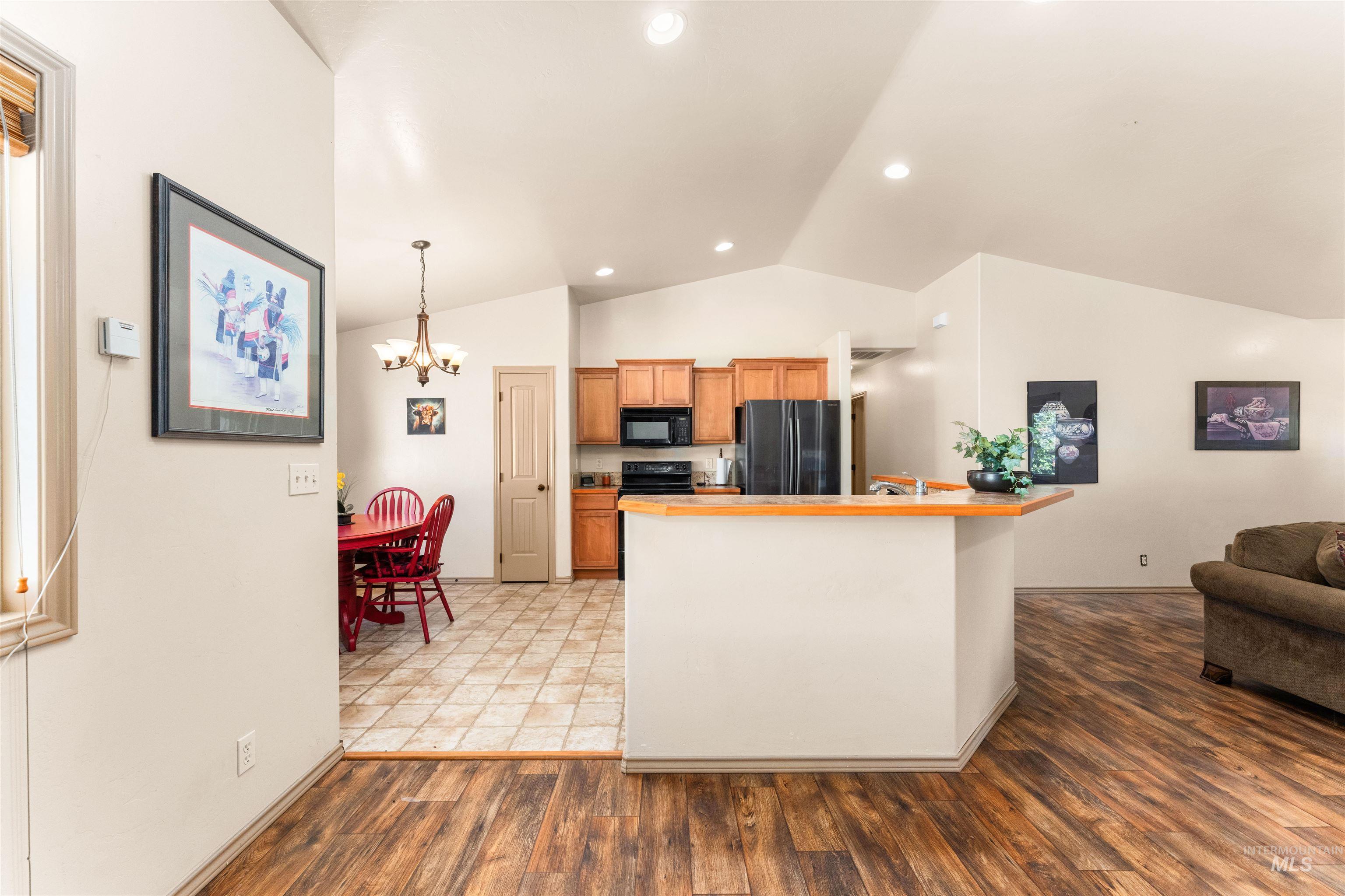 Kitchen with vaulted ceiling, a chandelier, black appliances, light wood-style floors, and open floor plan