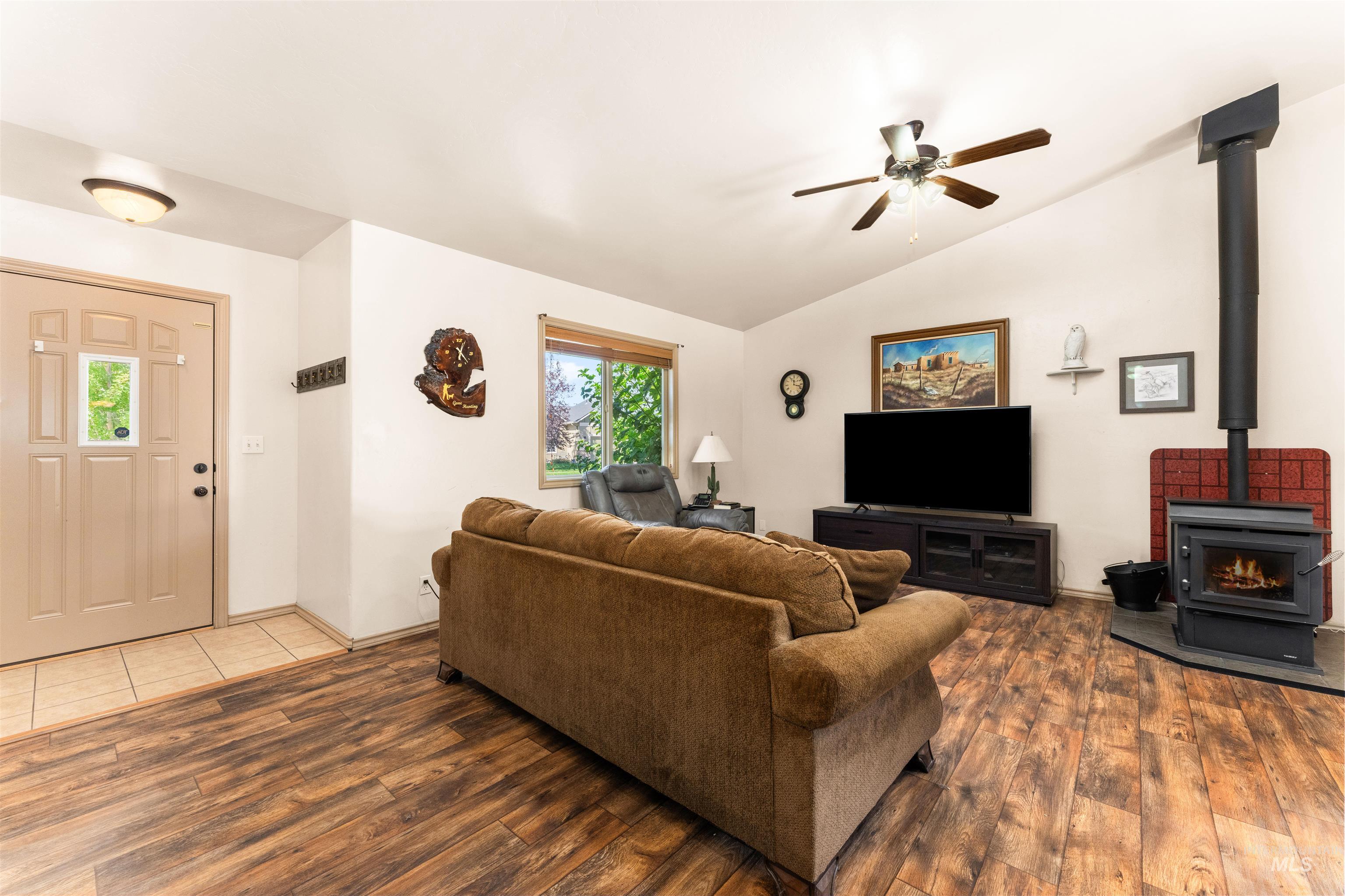 Living room with a wood stove, lofted ceiling, wood finished floors, and ceiling fan