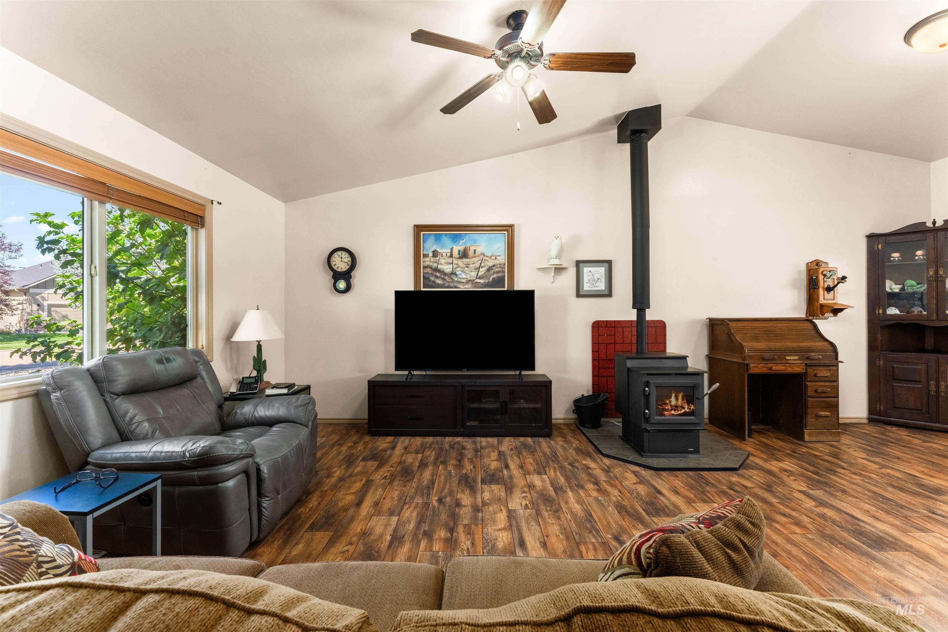Living area featuring a wood stove, lofted ceiling, wood finished floors, and a ceiling fan