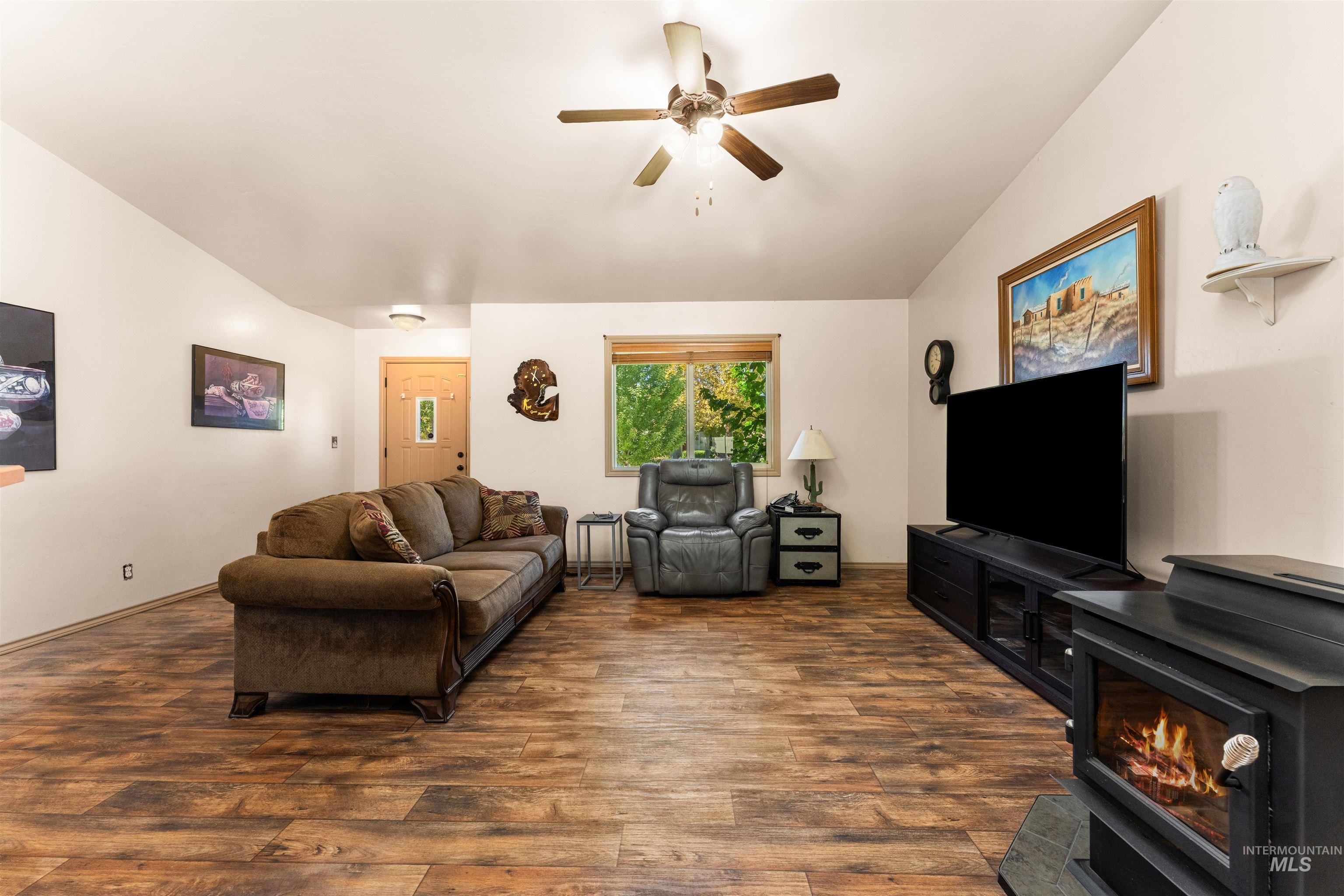 Living room featuring a wood stove, dark wood-style floors, a ceiling fan, and vaulted ceiling