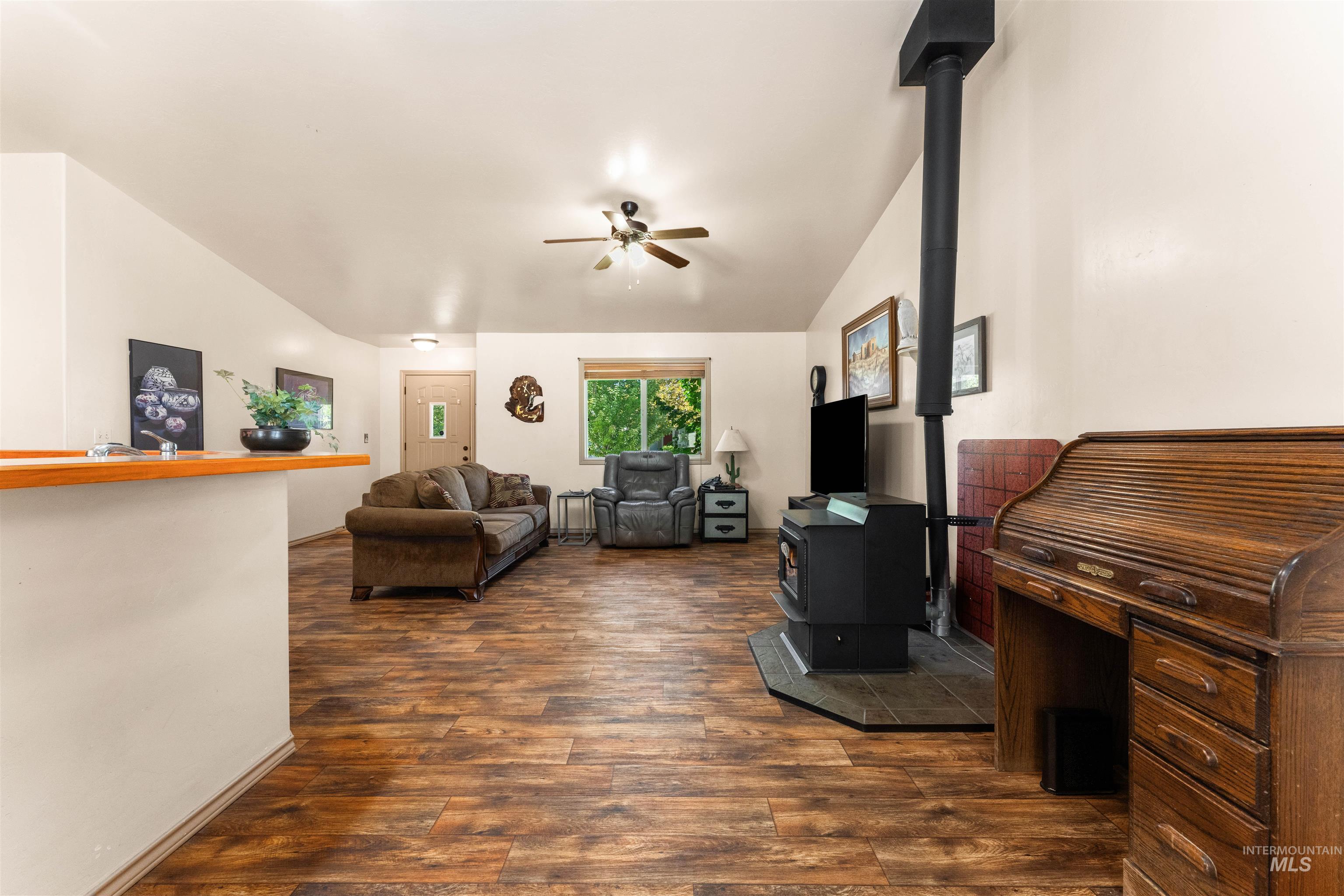Living room featuring a wood stove, dark wood-type flooring, vaulted ceiling, and a ceiling fan