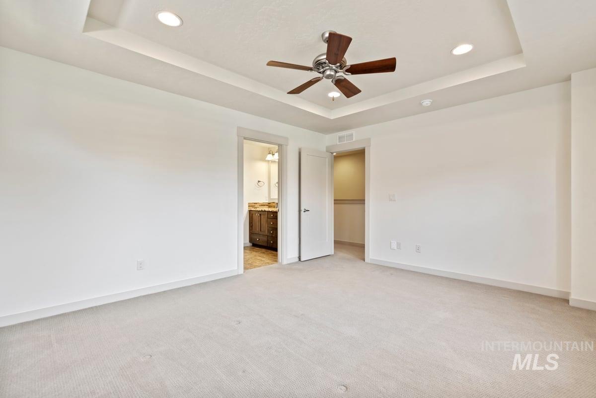 Unfurnished bedroom with a raised ceiling, light colored carpet, a ceiling fan, recessed lighting, and ensuite bathroom