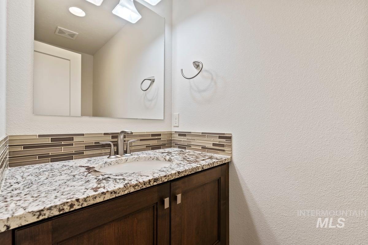 Bathroom with a textured wall, vanity, and tasteful backsplash