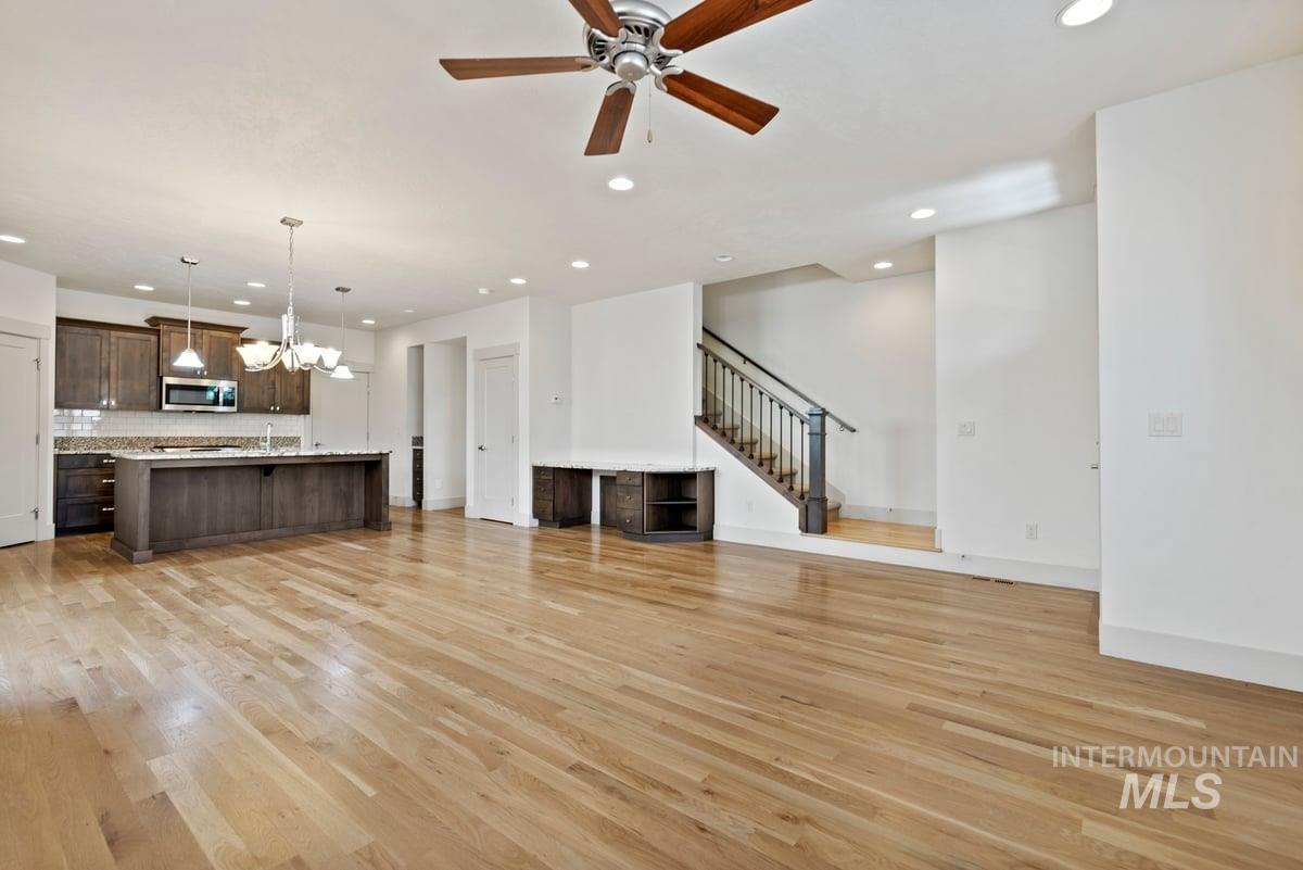 Unfurnished living room featuring stairs, a chandelier, light wood-style floors, recessed lighting, and a ceiling fan