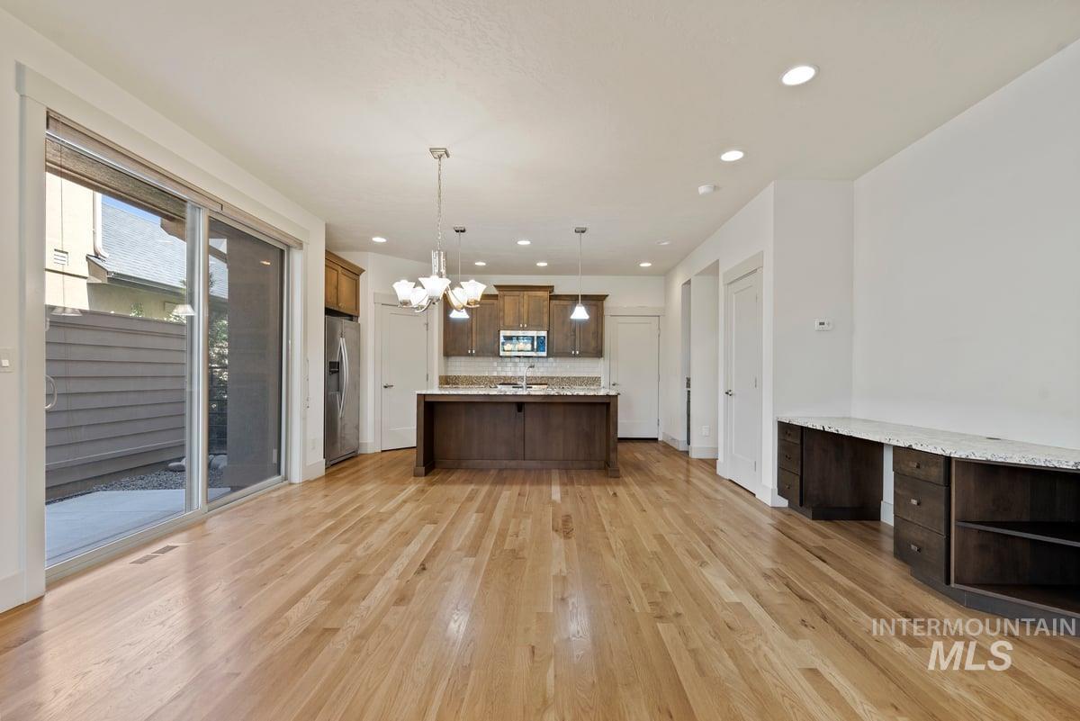 Kitchen featuring pendant lighting, a chandelier, open shelves, a center island with sink, and light wood-style flooring