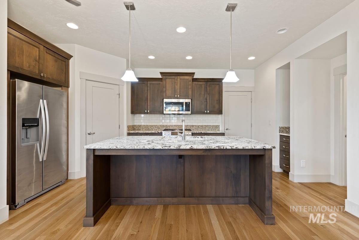 Kitchen featuring appliances with stainless steel finishes, dark brown cabinets, light stone counters, decorative backsplash, and recessed lighting