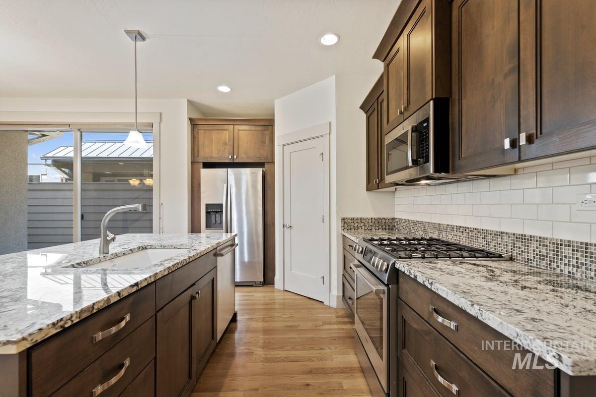 Kitchen featuring stainless steel appliances, hanging light fixtures, light wood-type flooring, recessed lighting, and light stone countertops