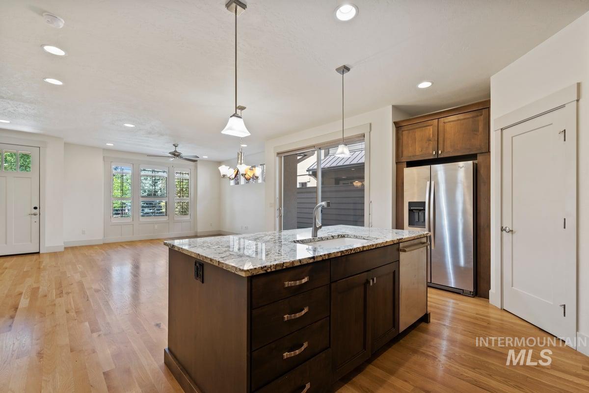 Kitchen featuring hanging light fixtures, stainless steel appliances, light stone countertops, recessed lighting, and open floor plan