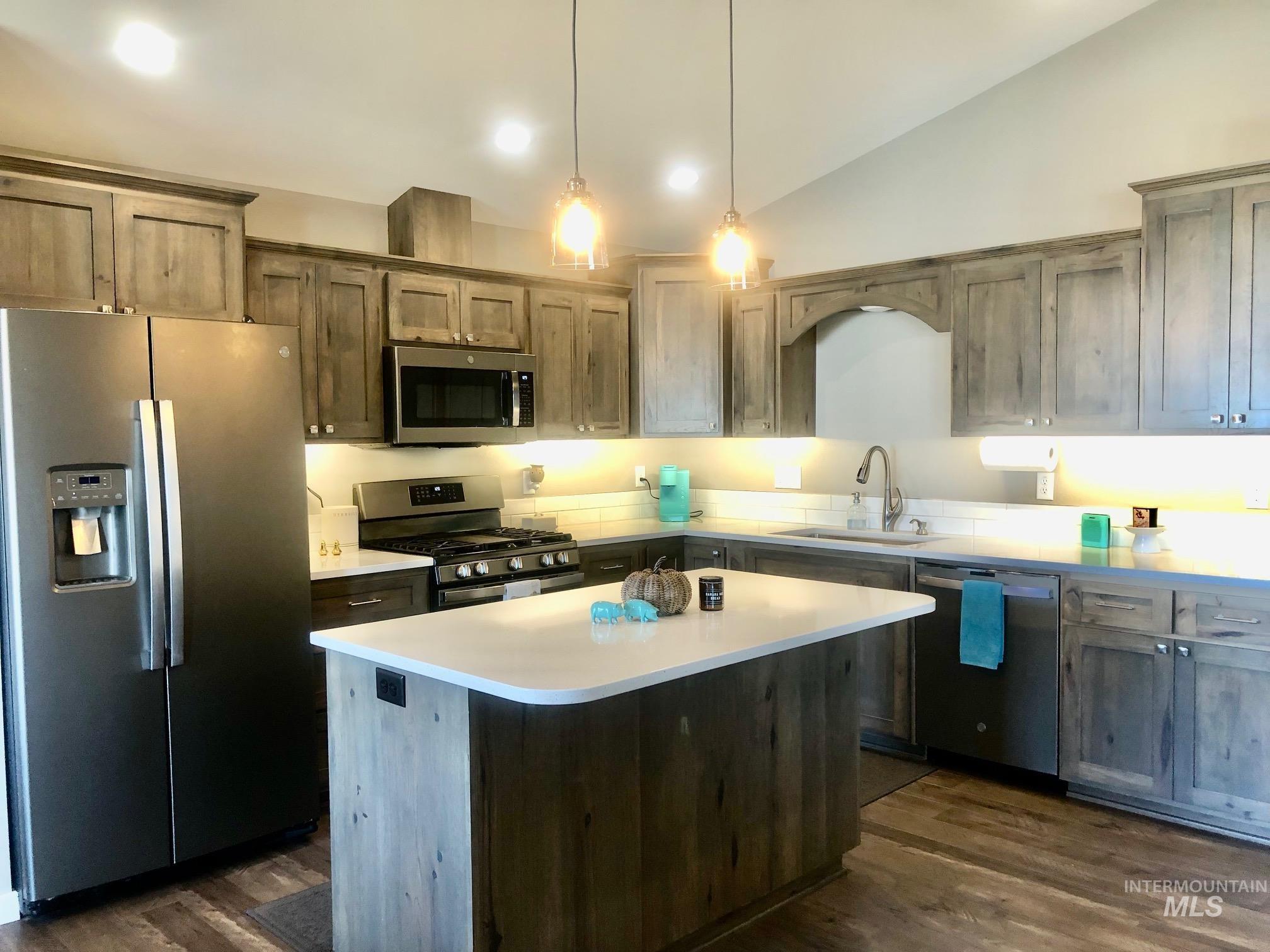 Kitchen with appliances with stainless steel finishes, lofted ceiling, a kitchen island, pendant lighting, and dark wood-type flooring