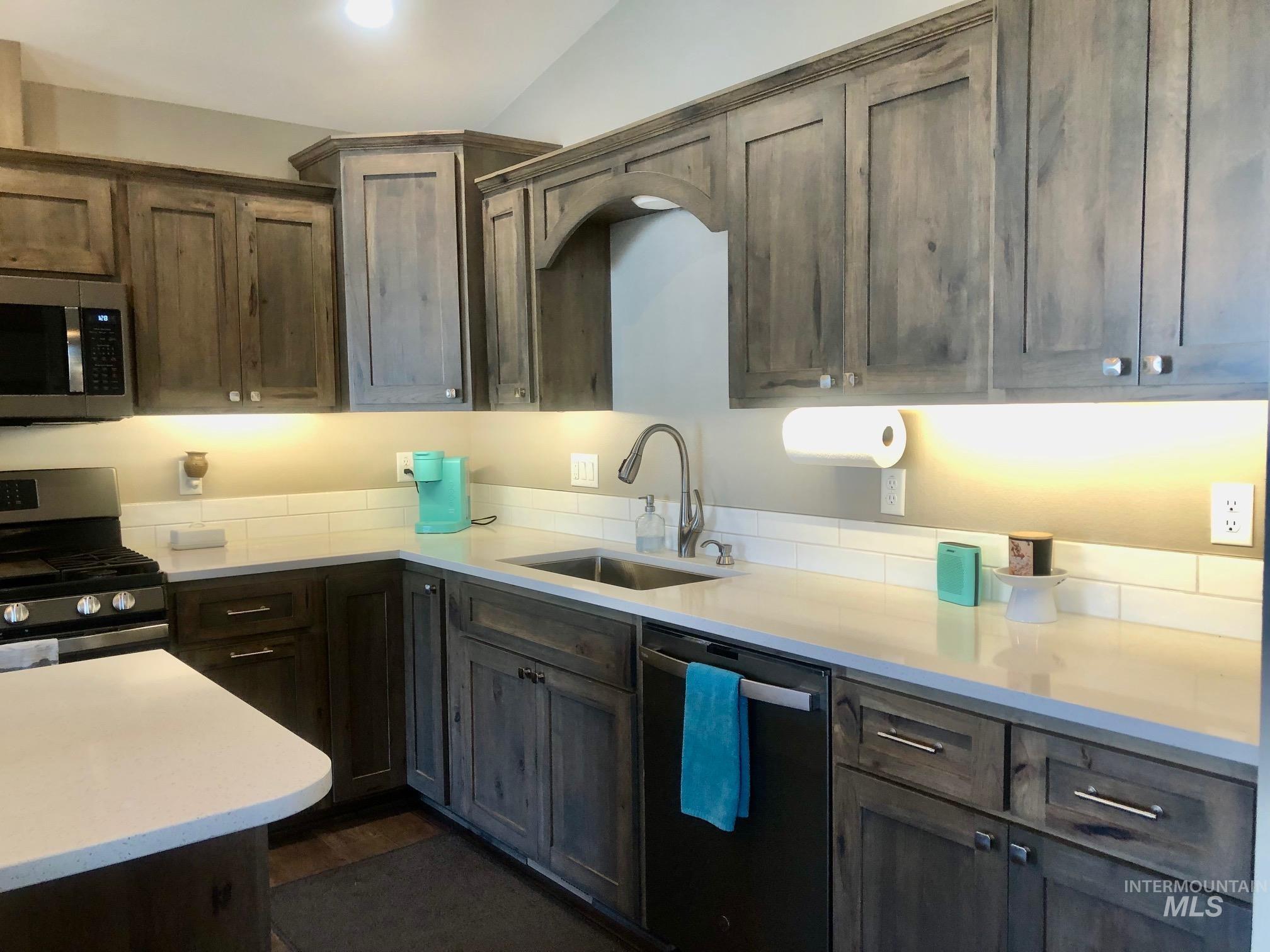 Kitchen featuring stainless steel appliances, light stone countertops, dark brown cabinetry, and vaulted ceiling