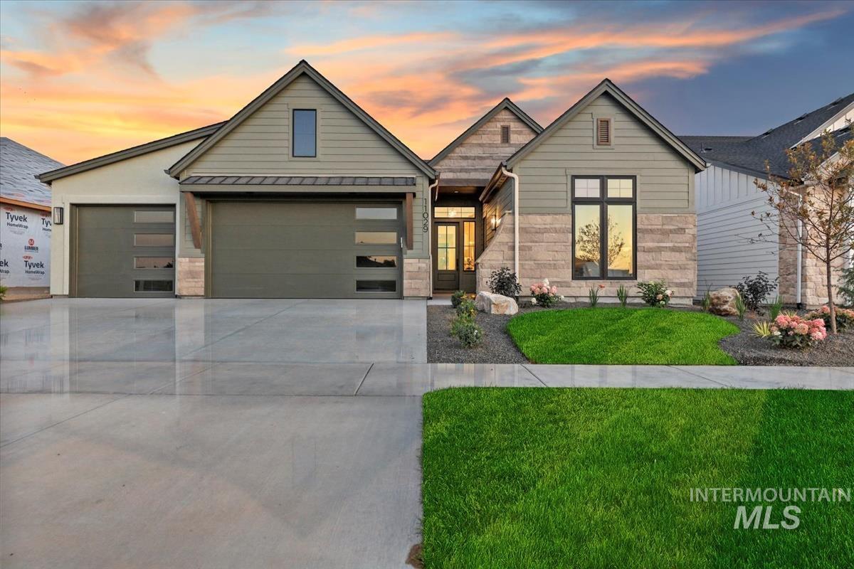 View of front of home featuring stone siding, a lawn, driveway, an attached garage, and a standing seam roof