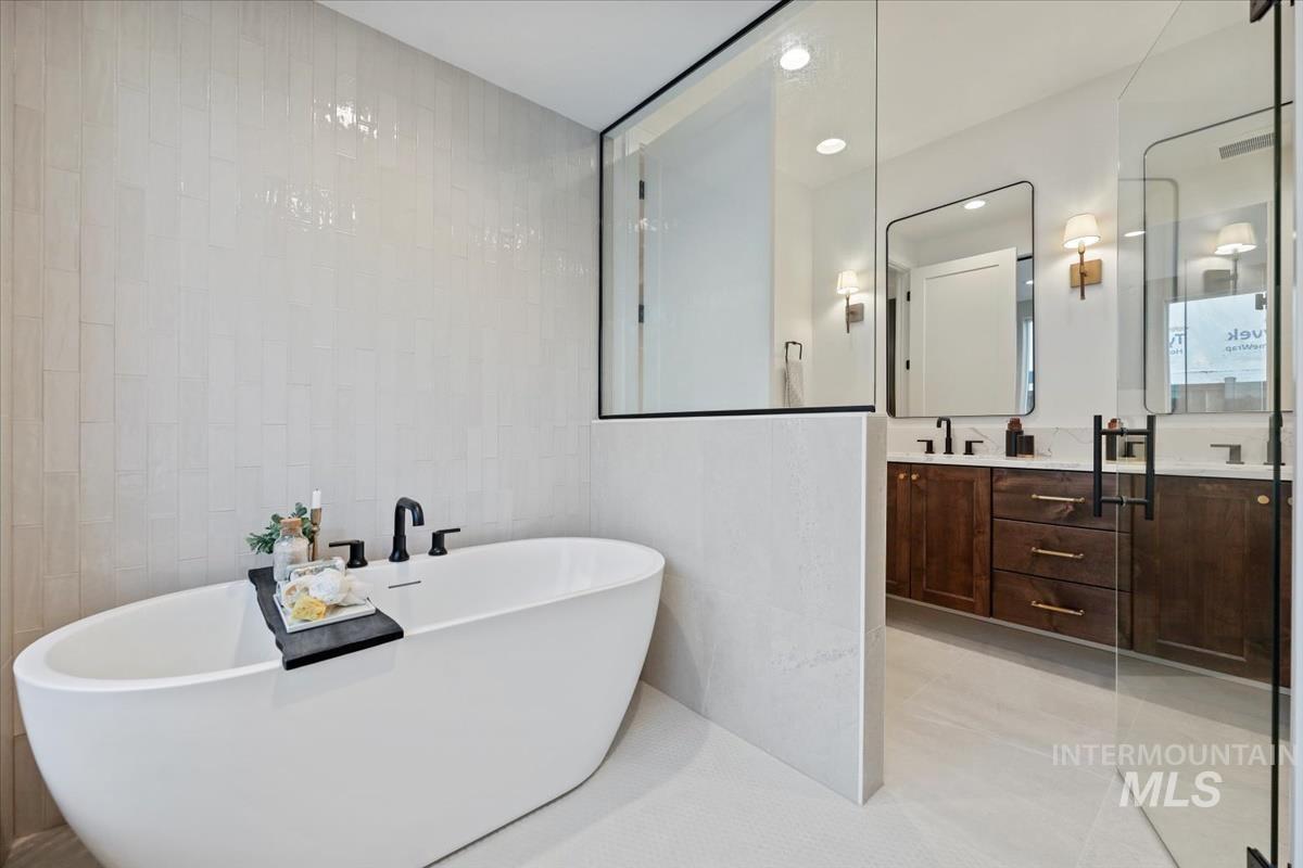 Full bathroom featuring double vanity, a soaking tub, tile walls, and light tile patterned floors
