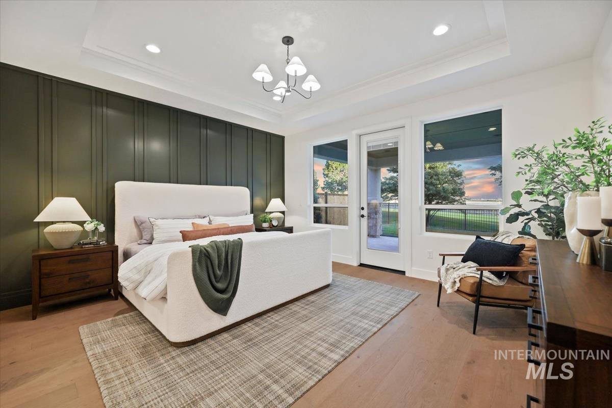Bedroom featuring a tray ceiling, light wood-style flooring, a chandelier, access to exterior, and recessed lighting