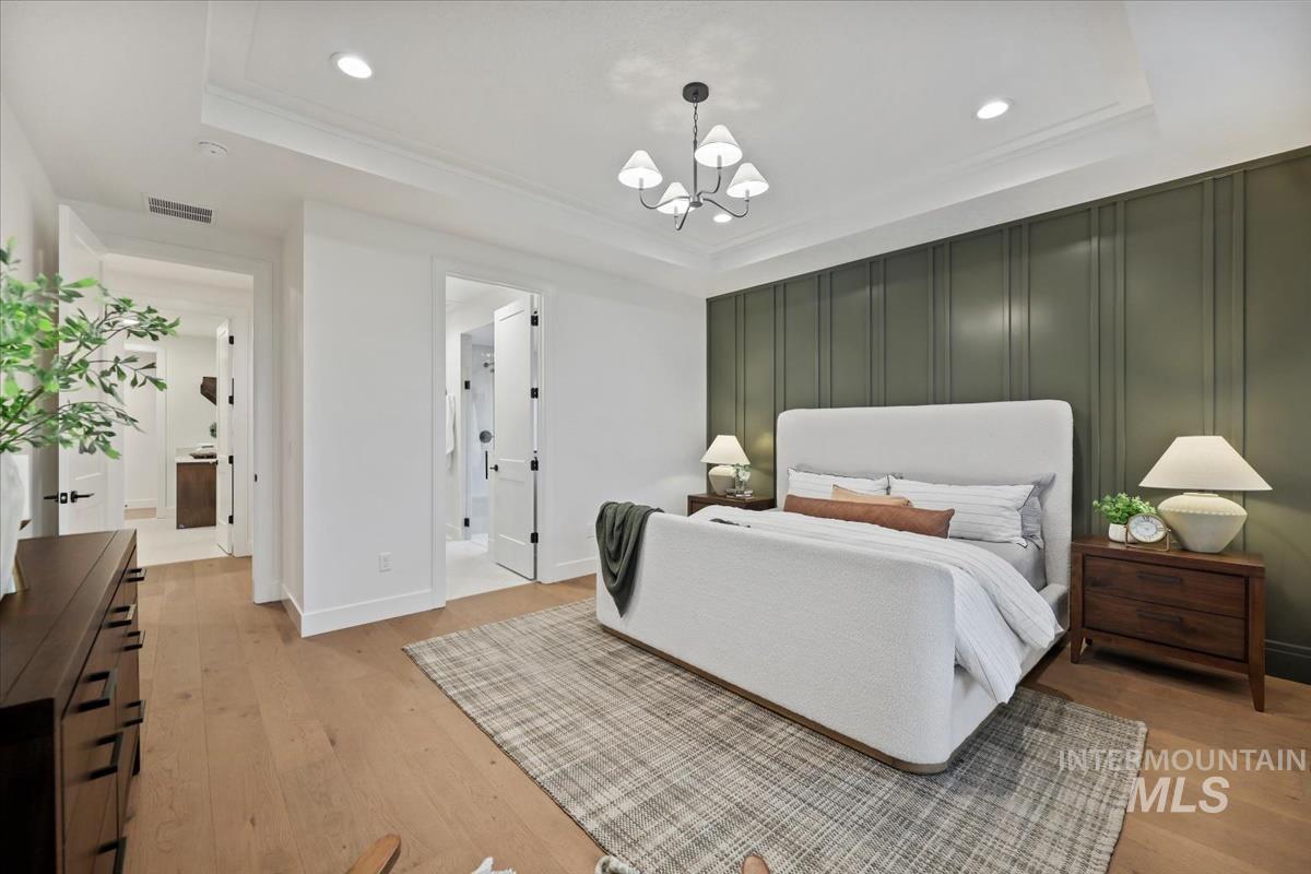 Bedroom with a tray ceiling, light wood-type flooring, a chandelier, ornamental molding, and recessed lighting