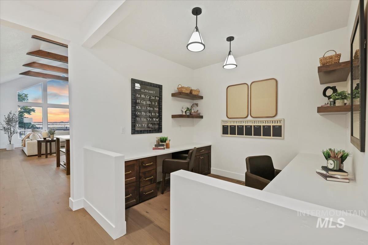 Home office featuring built in desk, light wood finished floors, and beamed ceiling