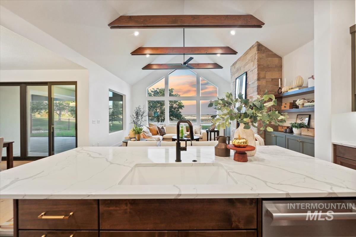 Kitchen with dark brown cabinets, light stone countertops, a center island with sink, dishwasher, and open floor plan