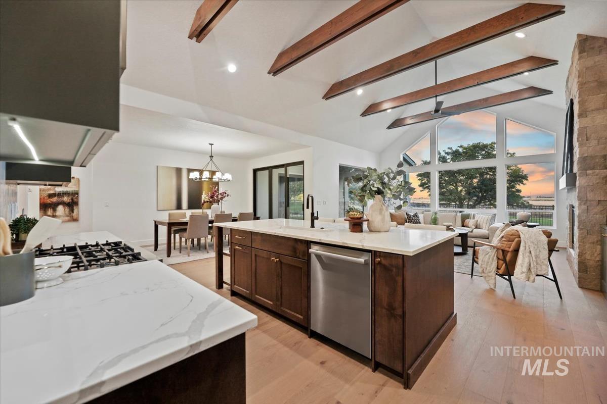 Kitchen featuring beam ceiling, decorative light fixtures, light wood-type flooring, light stone counters, and dishwasher