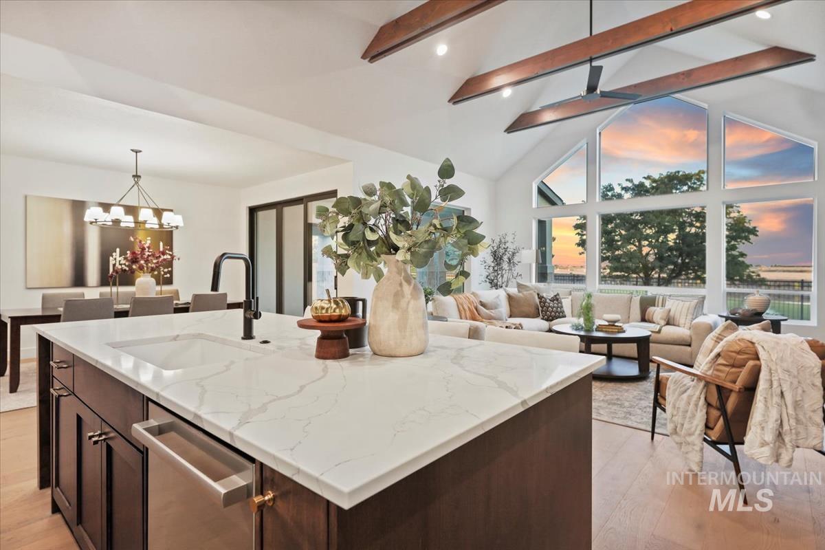 Kitchen featuring beamed ceiling, light stone counters, dark brown cabinetry, open floor plan, and decorative light fixtures