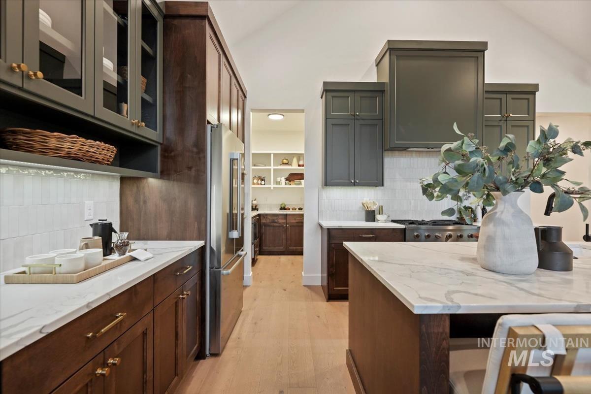 Kitchen with glass insert cabinets, light wood finished floors, light stone countertops, high quality fridge, and decorative backsplash