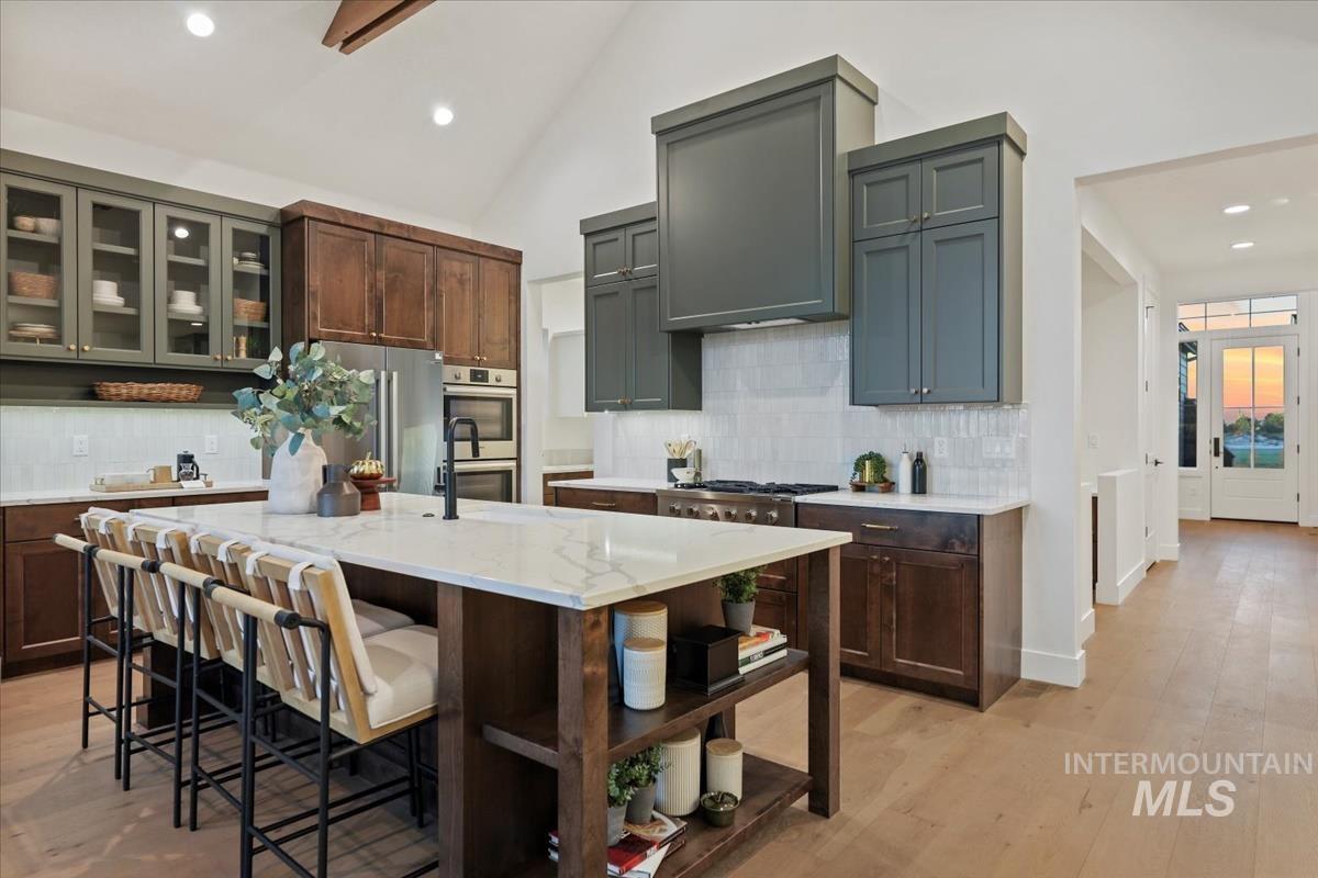 Kitchen with backsplash, recessed lighting, glass insert cabinets, light wood-style floors, and a center island with sink