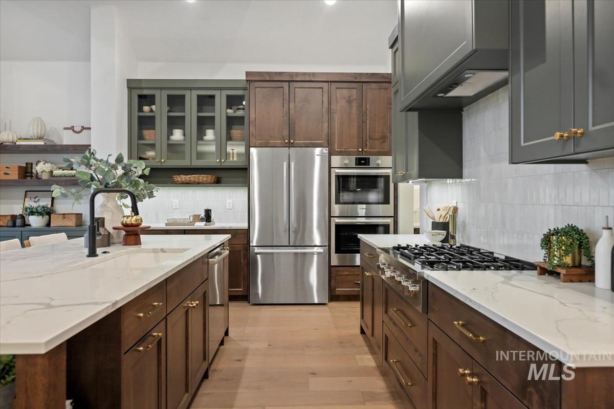 Kitchen with appliances with stainless steel finishes, light wood-type flooring, glass insert cabinets, and light stone countertops
