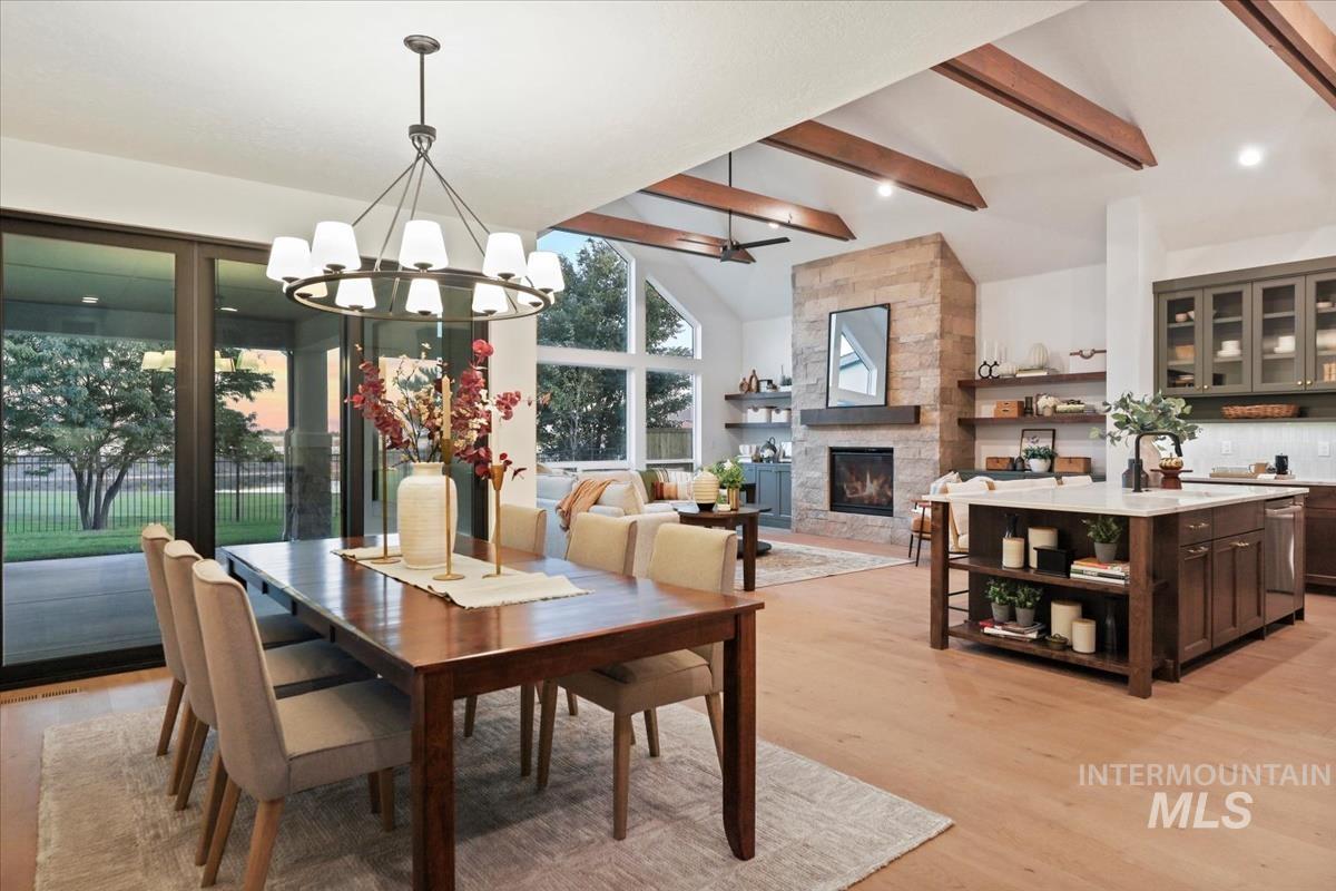 Dining room with beamed ceiling, light wood finished floors, a stone fireplace, a chandelier, and high vaulted ceiling