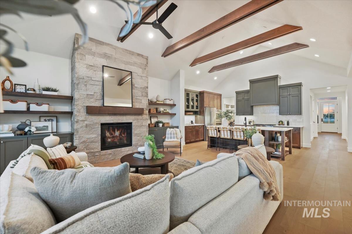 Living room featuring beamed ceiling, light wood-type flooring, ceiling fan, a stone fireplace, and recessed lighting