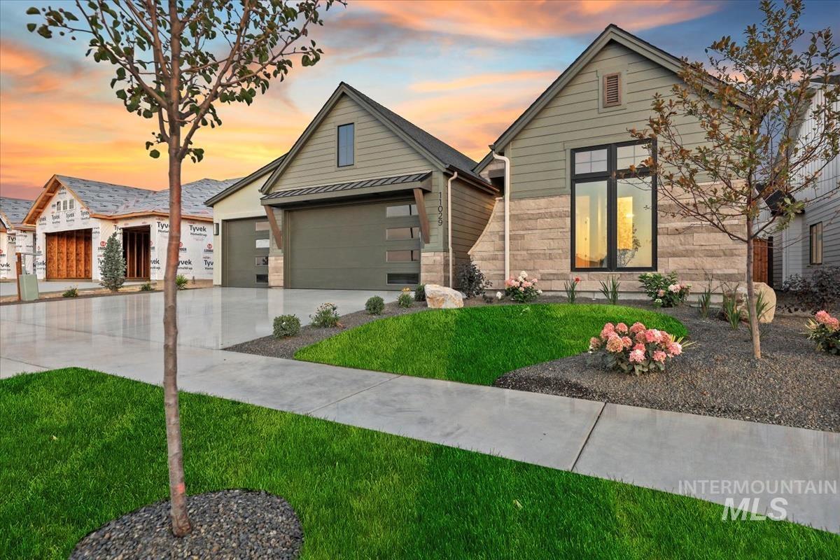 View of front of house with a yard, concrete driveway, a garage, stone siding, and a metal roof