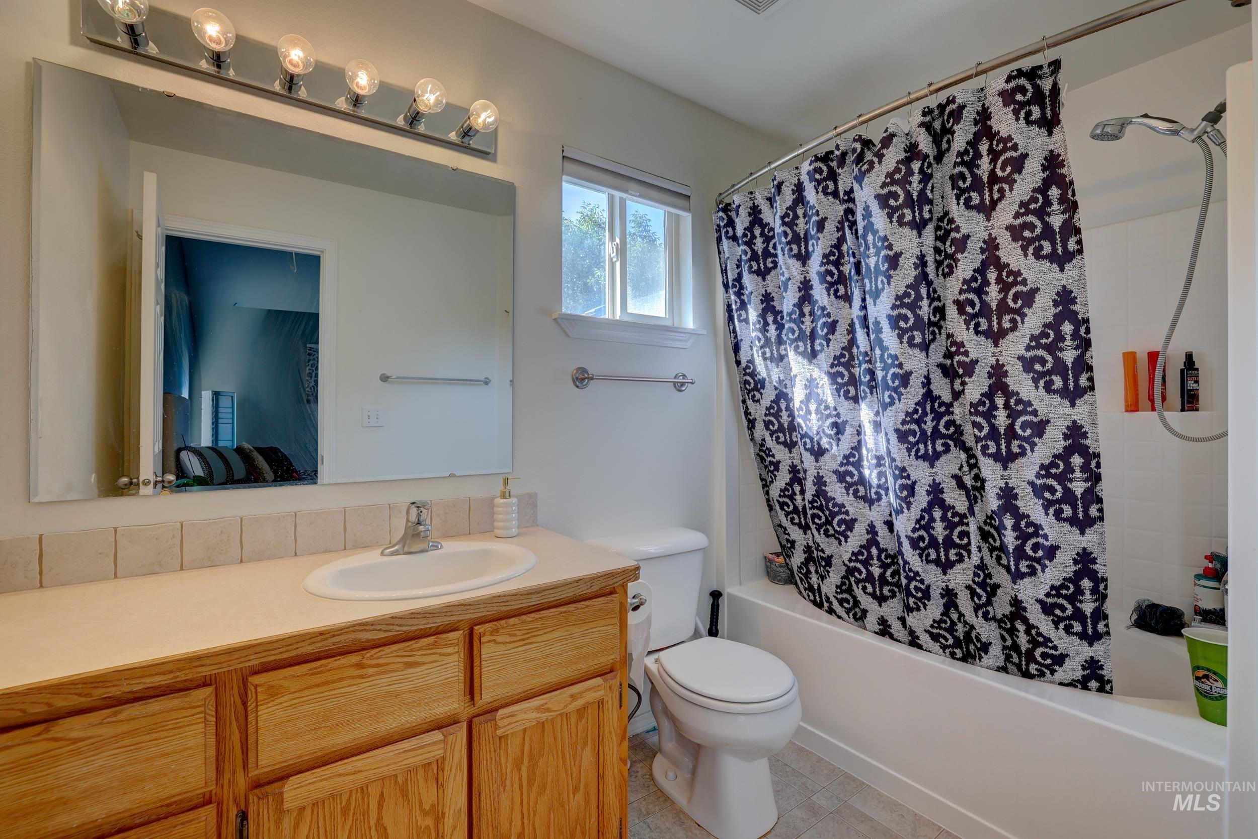 Ensuite bathroom featuring shower / bath combination with curtain, vanity, and light tile patterned floors