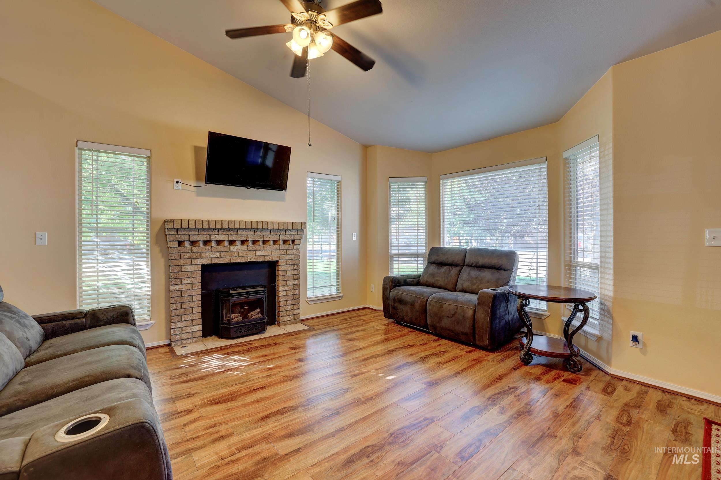 Living room with lofted ceiling, light wood-style floors, a wood stove, and a ceiling fan