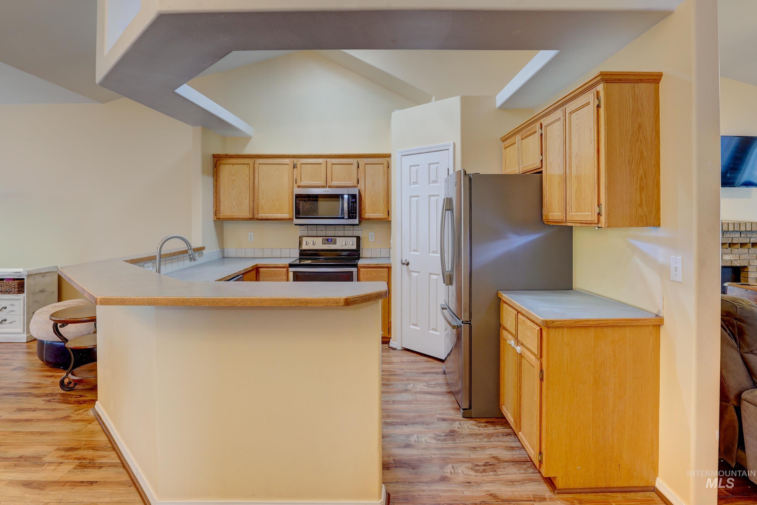 Kitchen featuring light countertops, appliances with stainless steel finishes, light wood-style floors, and a peninsula