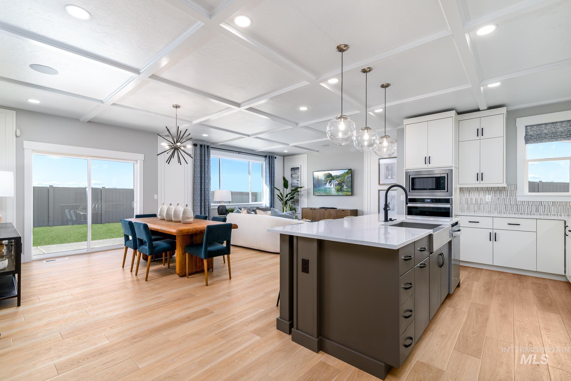 Kitchen featuring white cabinets, light wood finished floors, pendant lighting, an island with sink, and tasteful backsplash