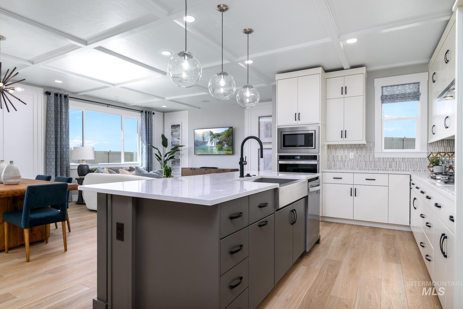 Kitchen featuring white cabinets, light wood finished floors, an island with sink, hanging light fixtures, and light stone countertops