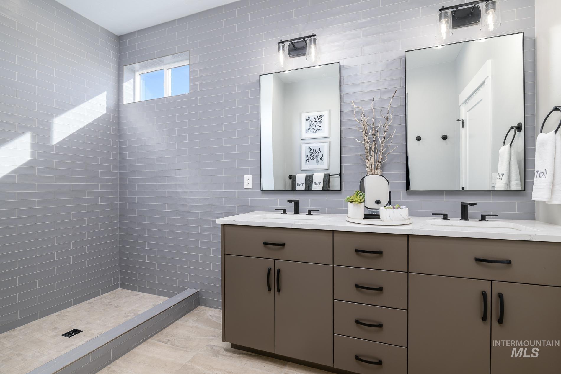 Full bathroom featuring double vanity, a stall shower, decorative backsplash, and tile walls