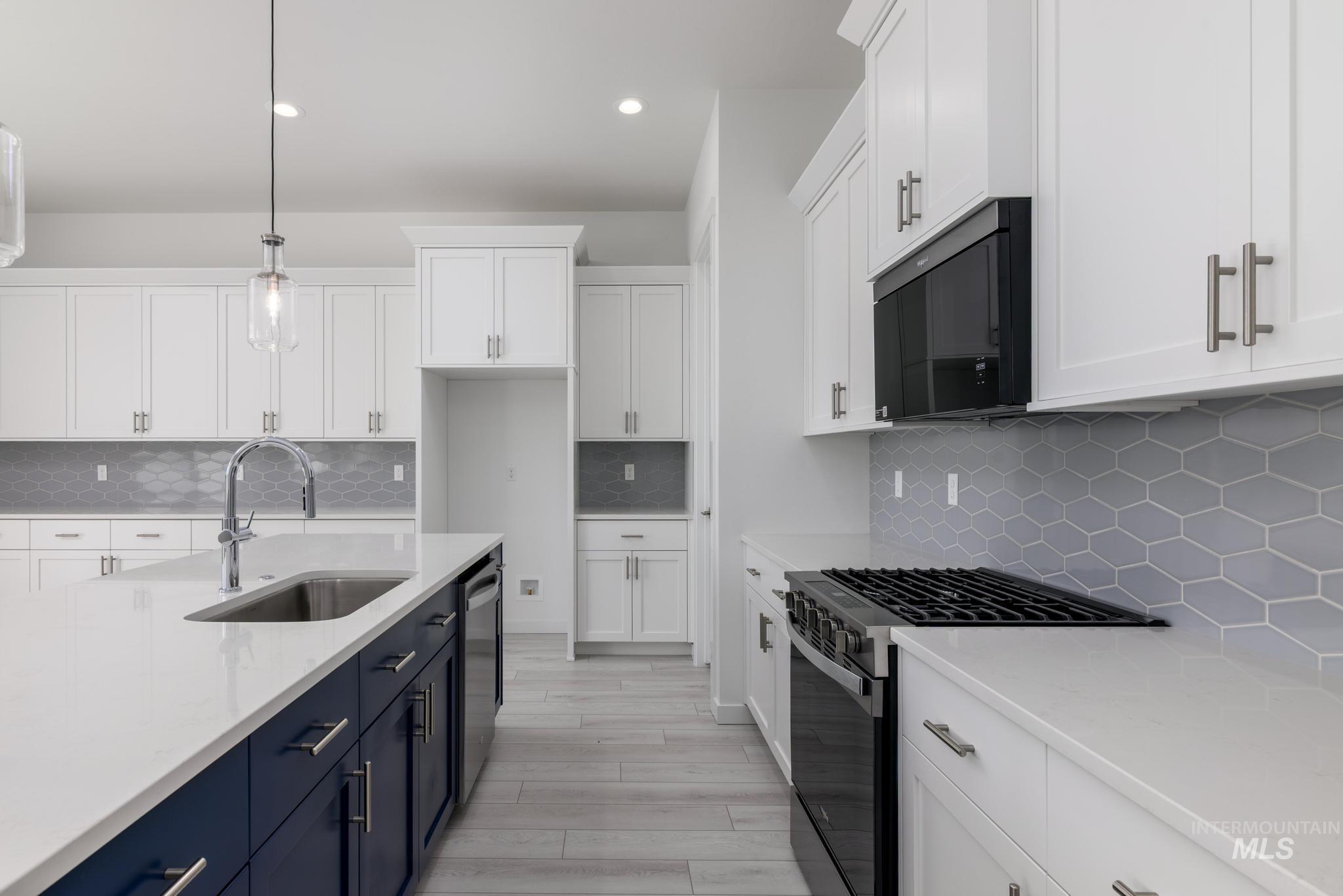 Kitchen with hanging light fixtures, range with gas stovetop, white cabinets, and recessed lighting