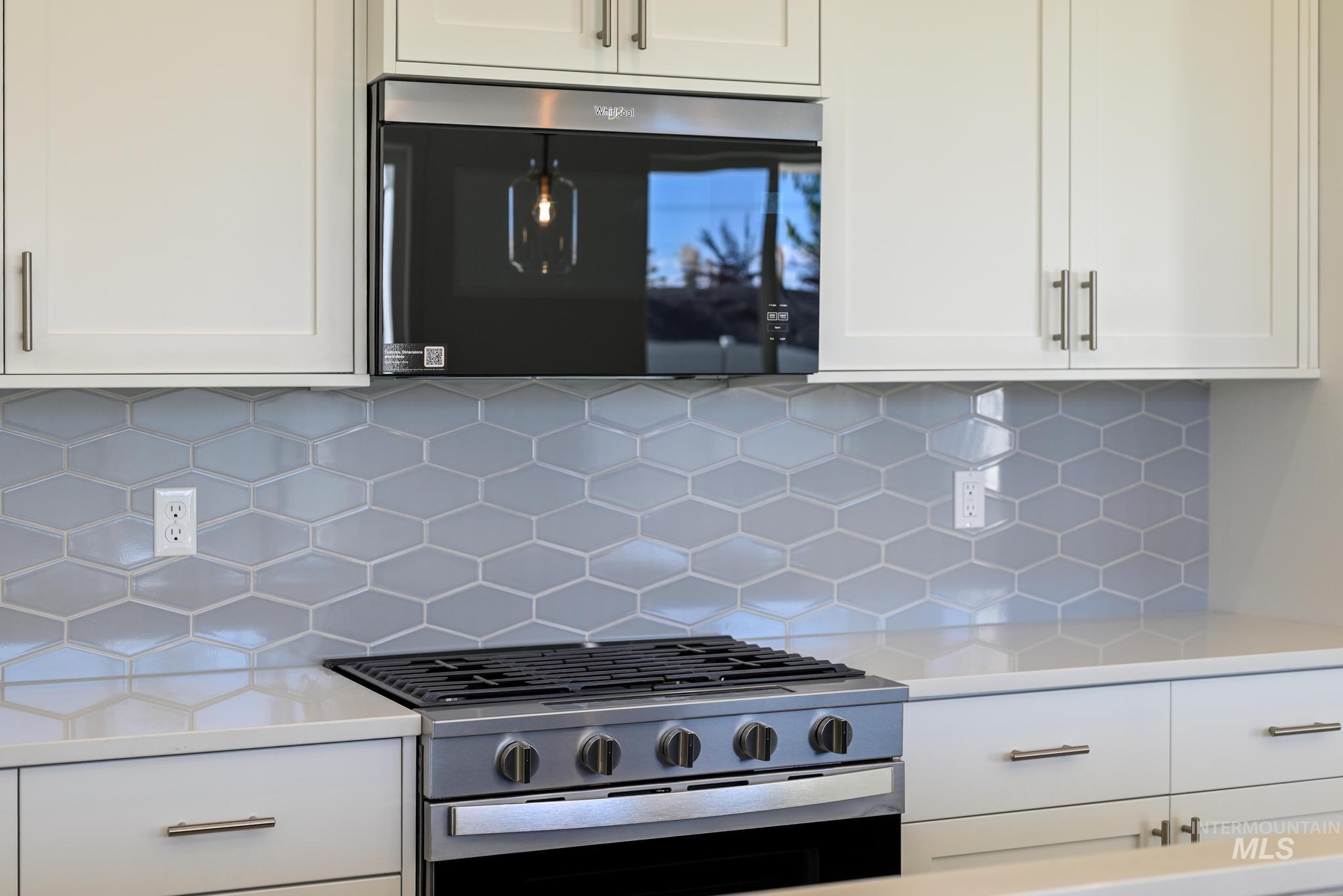 Kitchen with appliances with stainless steel finishes, white cabinetry, tasteful backsplash, and light stone countertops